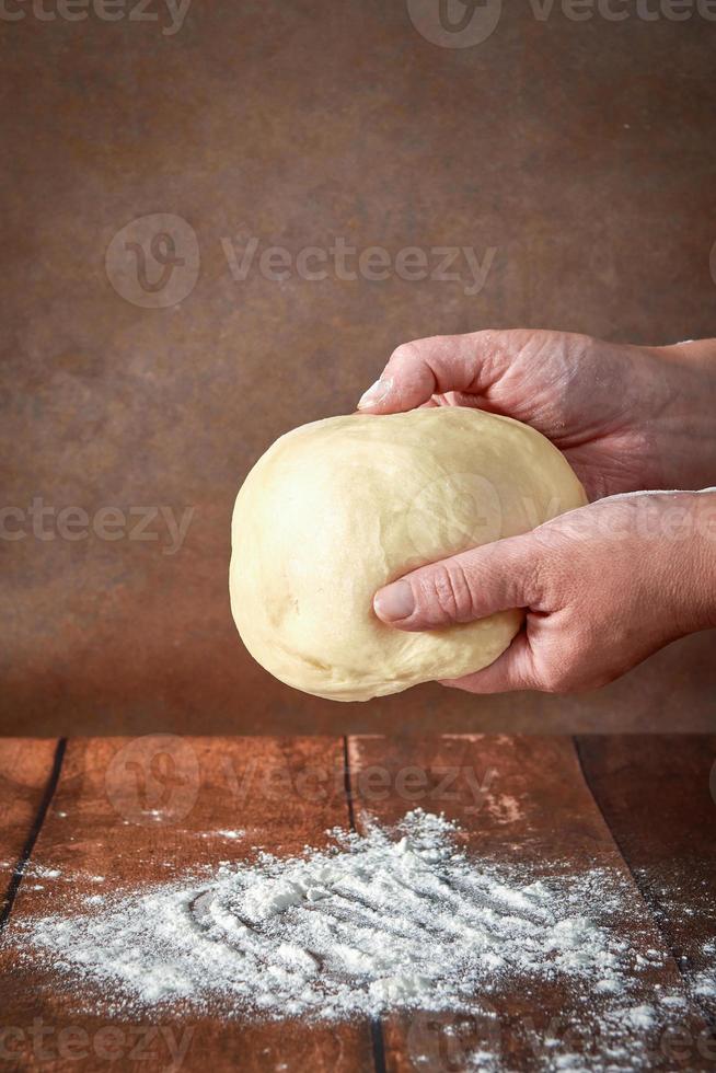 The hands of an elderly, plump woman are kneading dough on a wooden table. Preparation of dough for a festive cake, pizza photo