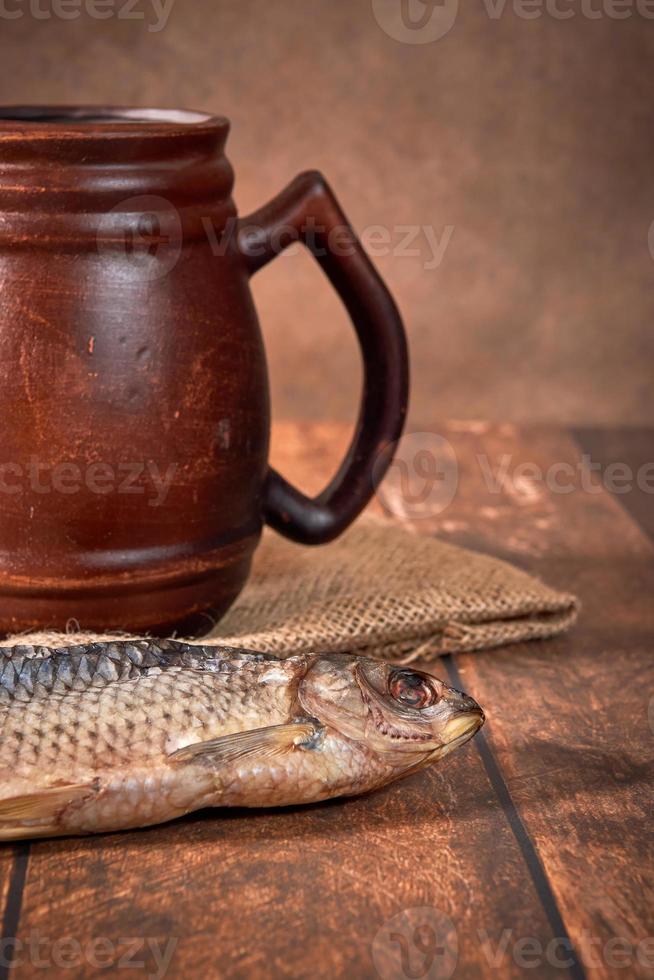 Beer clay brown mug with beer and dried fish on a wooden table on a dark background. photo