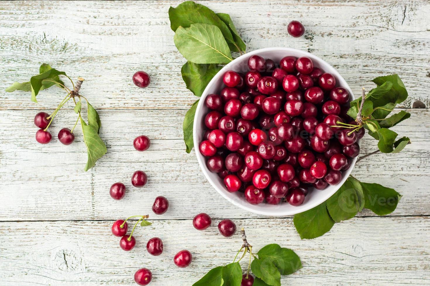 tazón blanco de cerezas dulces frescas con hojas en gotas de agua sobre fondo de madera foto