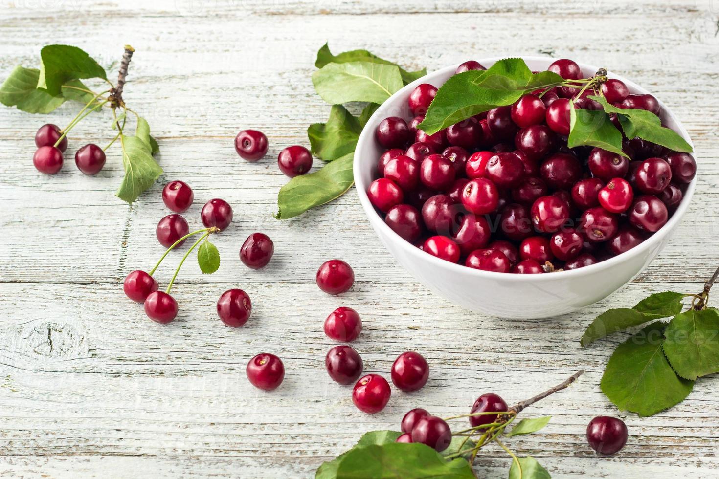 tazón blanco de cerezas dulces frescas con hojas en gotas de agua sobre fondo de madera foto