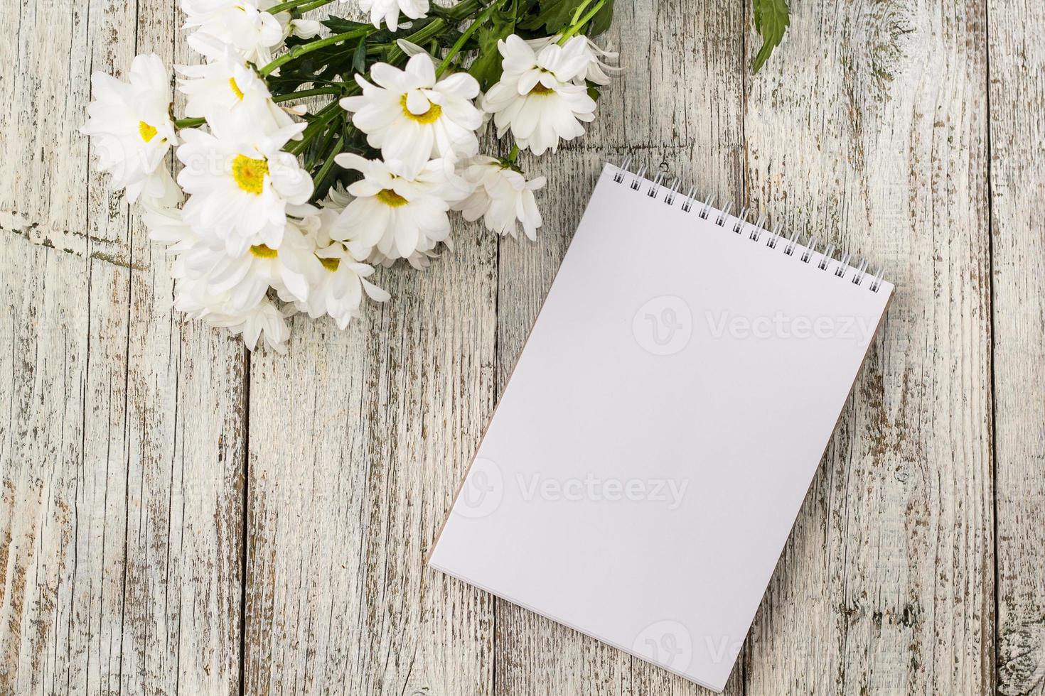 spring bouquet of white daisies with clean notebook to write on white wooden table photo