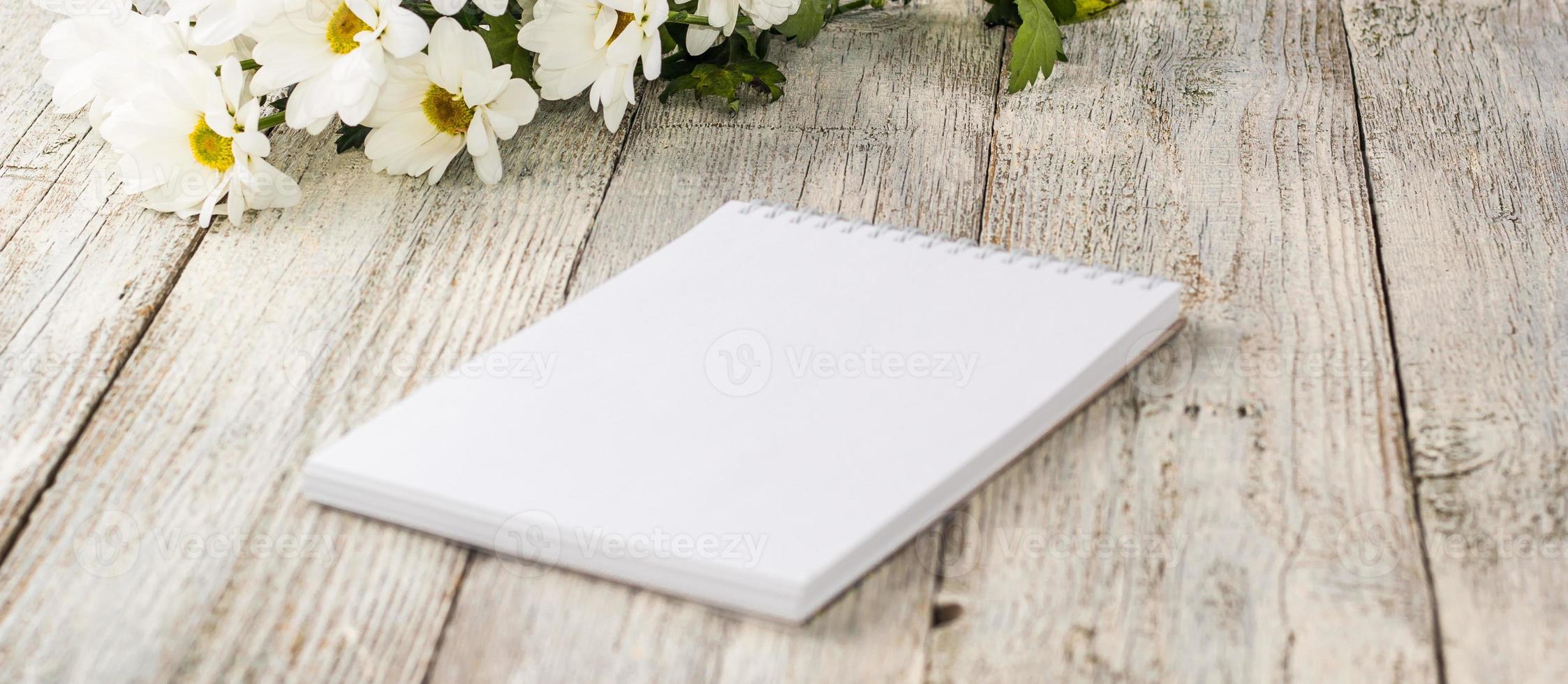 spring bouquet of white daisies with clean notebook to write on white wooden table photo