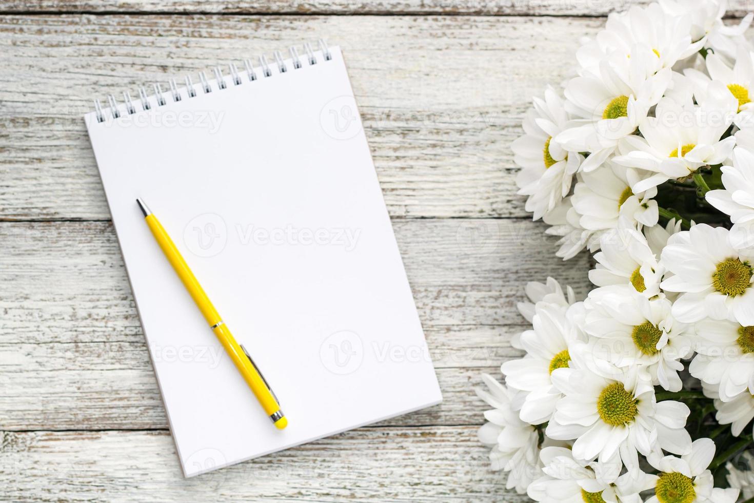 spring bouquet of white daisies with clean notebook to write on white wooden table photo