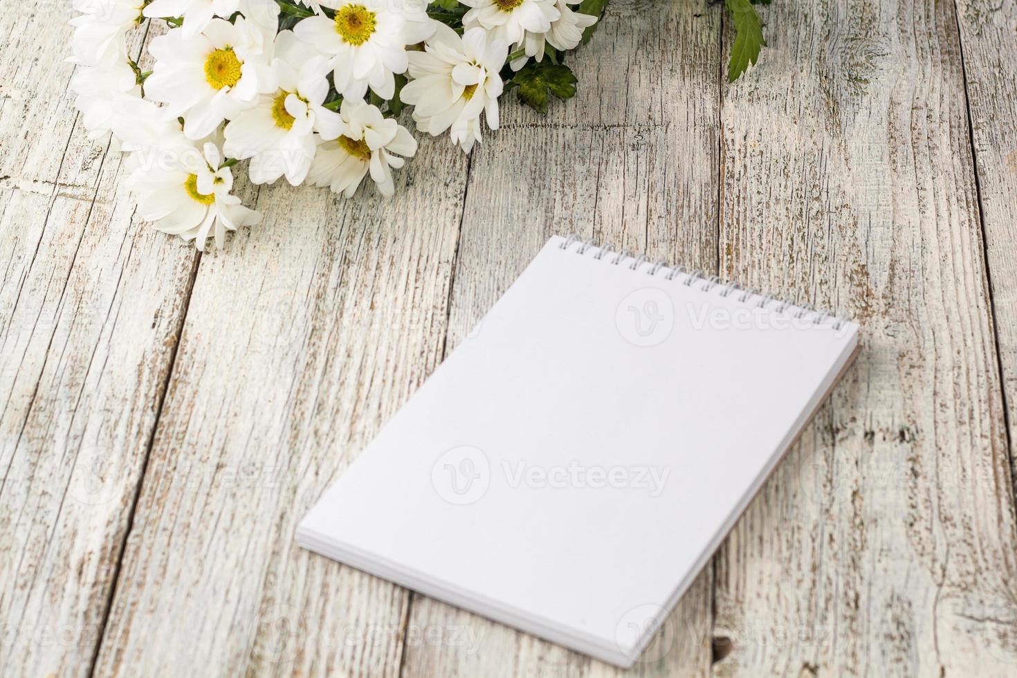 spring bouquet of white daisies with clean notebook to write on white wooden table photo