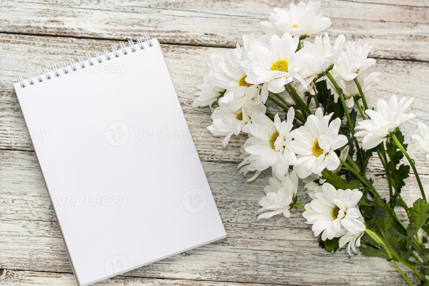 spring bouquet of white daisies with clean notebook to write on white wooden table photo
