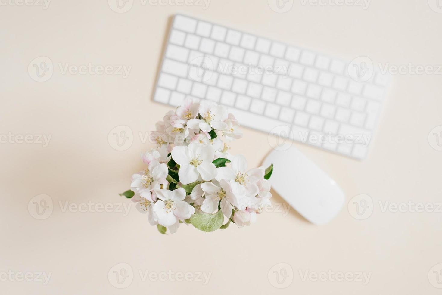 Keyboard and mouse and white apple flowers in a vase out of focus on a beige table. Layout and design concept. Flat lay. photo