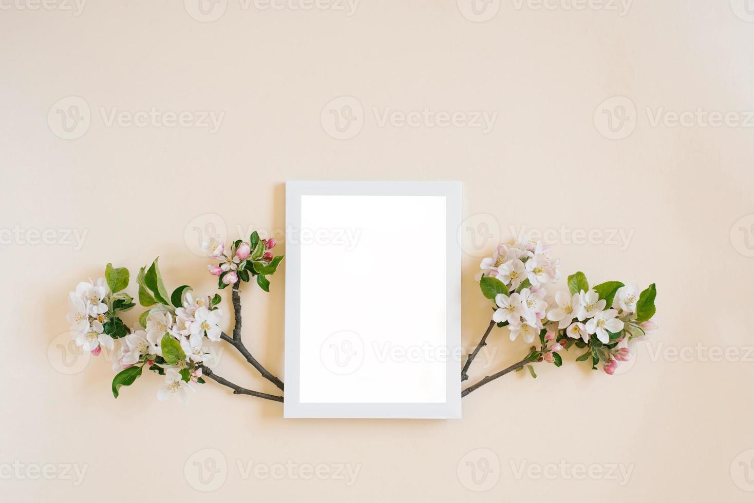 White frame with copy space on a beige background surrounded by branches with white apple flowers photo