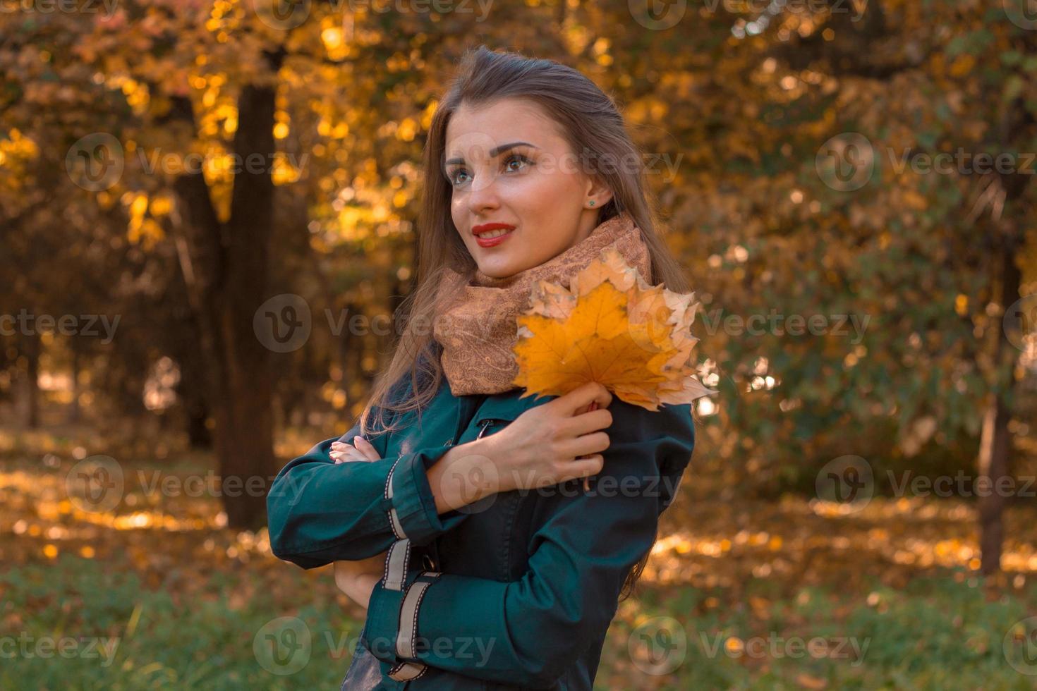 niña con hojas en la mano vale la pena en el parque de otoño y mira hacia otro lado foto