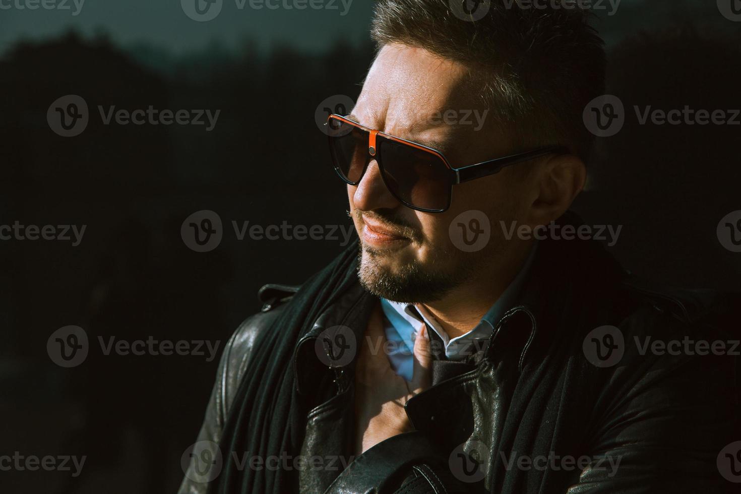 Serious man in sunglasses looking away near black wall photo