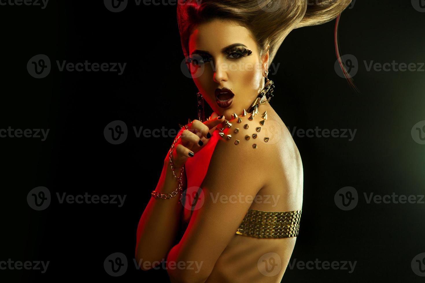 Seduction young girl with creative hairstyle and golden accessories in studio photo