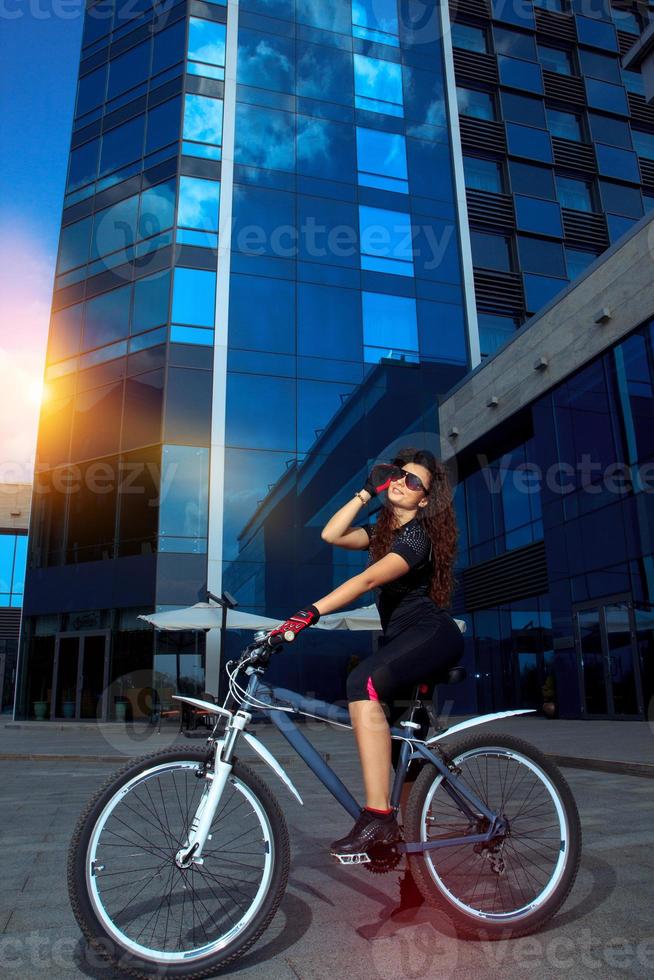 mujer deportiva morena con gafas de sol posando en bicicleta foto