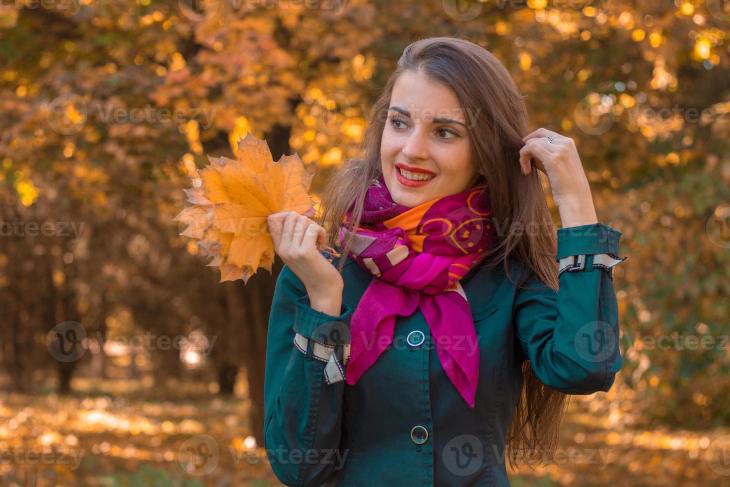 smiling pretty girl in pink scarf stands in the Park clings to the hair while the other hand holds the leaves photo