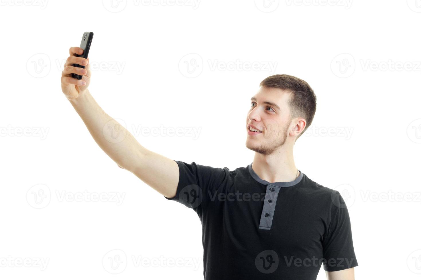un joven sonriente con la camisa negra levantó la mano y hace una foto por teléfono