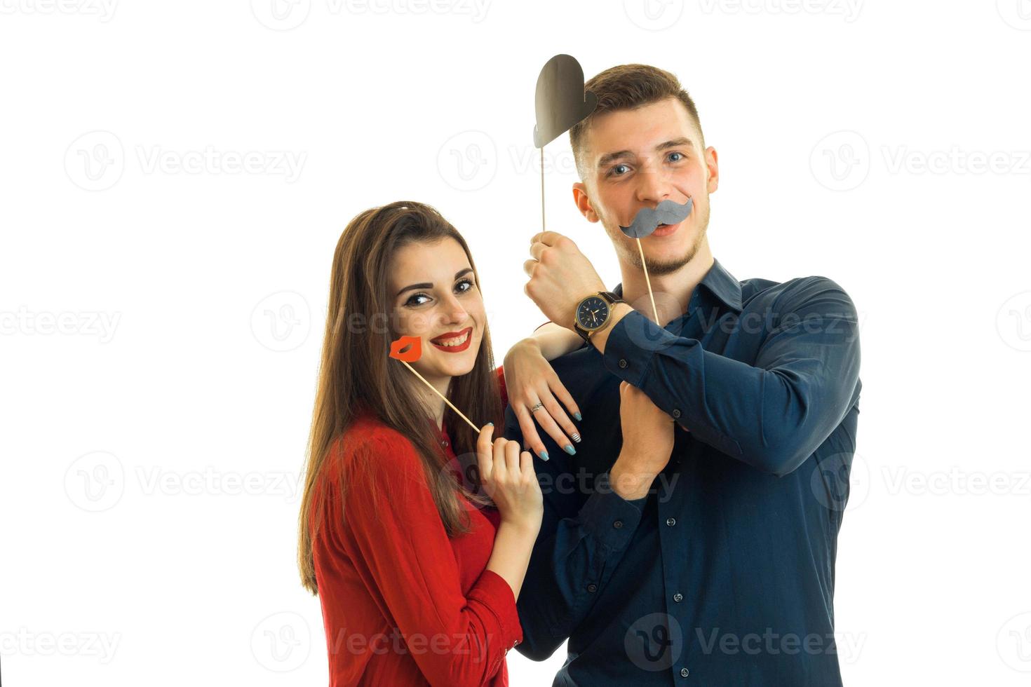 young smiling guy with girl, hold near face paper props in the form of lips, moustache and hats for a photo