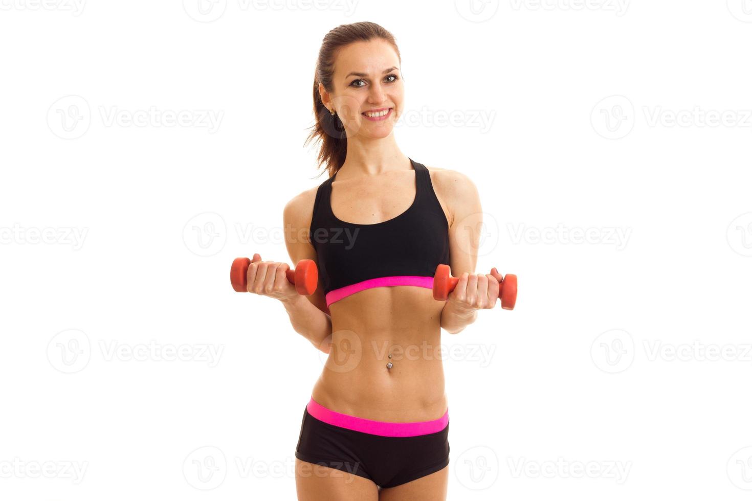 young smiling female athlete stands in front of the camera at the top and shorts and holding a dumbbell photo
