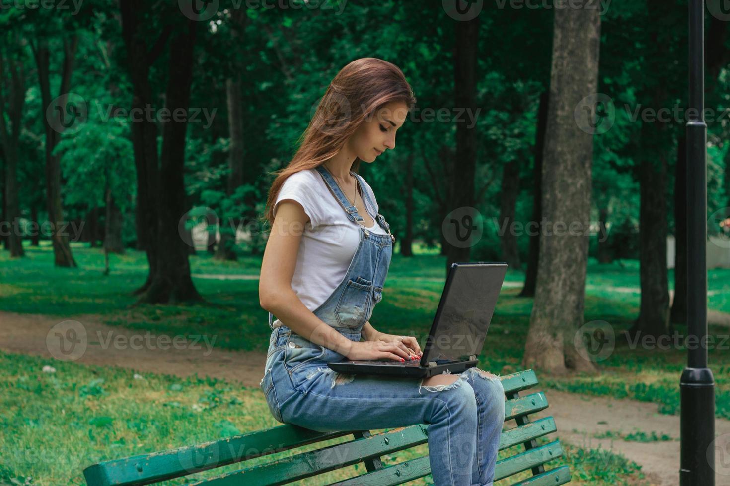 una joven morena se sienta en un banco y trabaja con una laptop foto