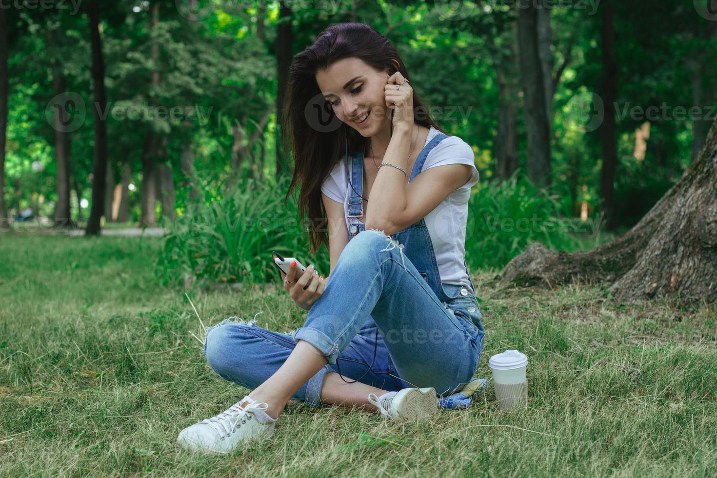 happy pretty girl sits on the grass smiles and listens to music photo