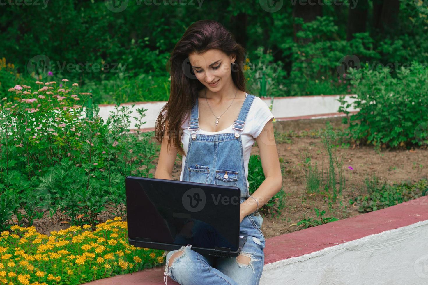 smiling young girl sits in the Park and prints on a laptop photo