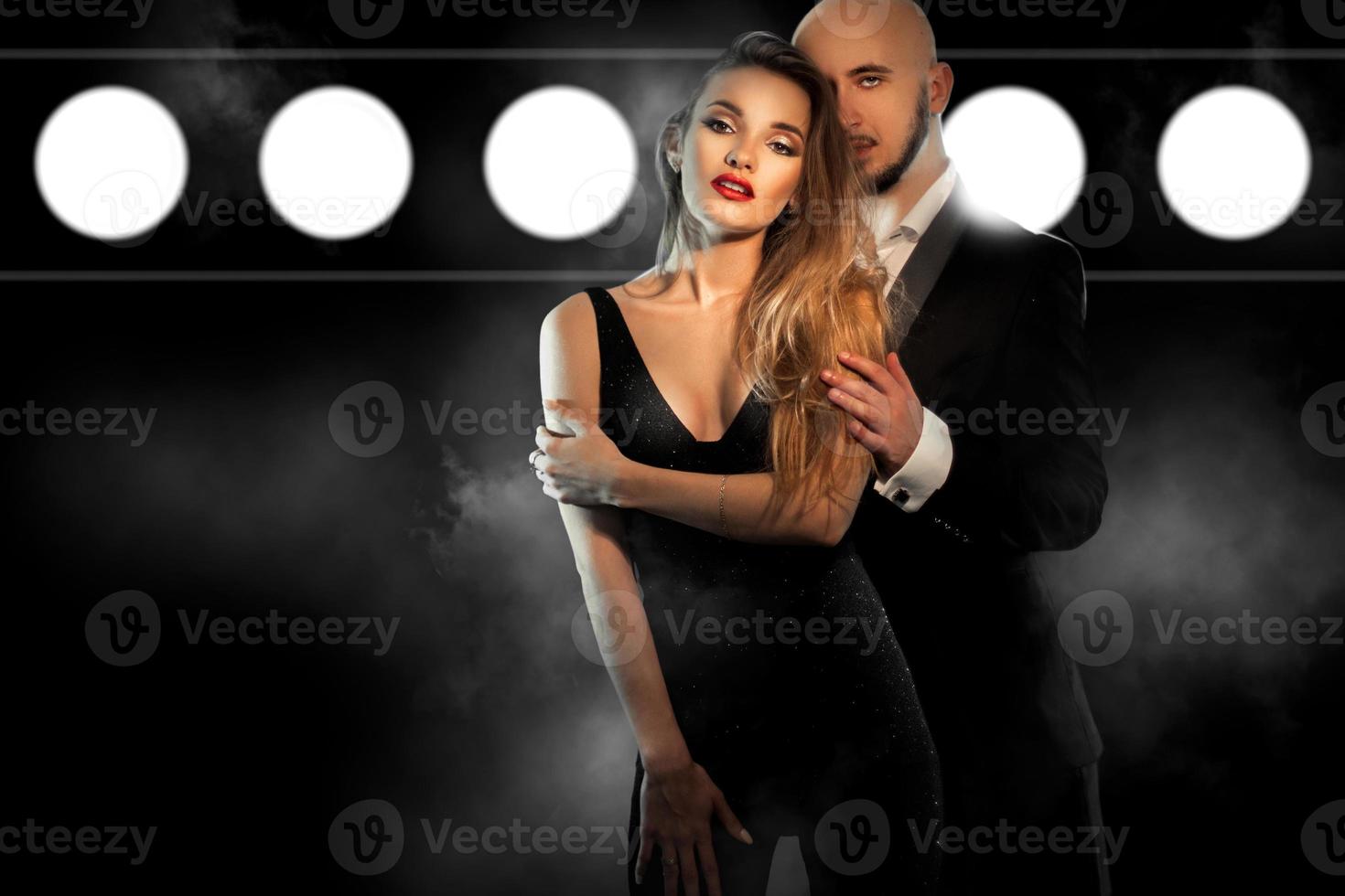 sexy young couple in black suit hugs and looks at the camera in studio photo