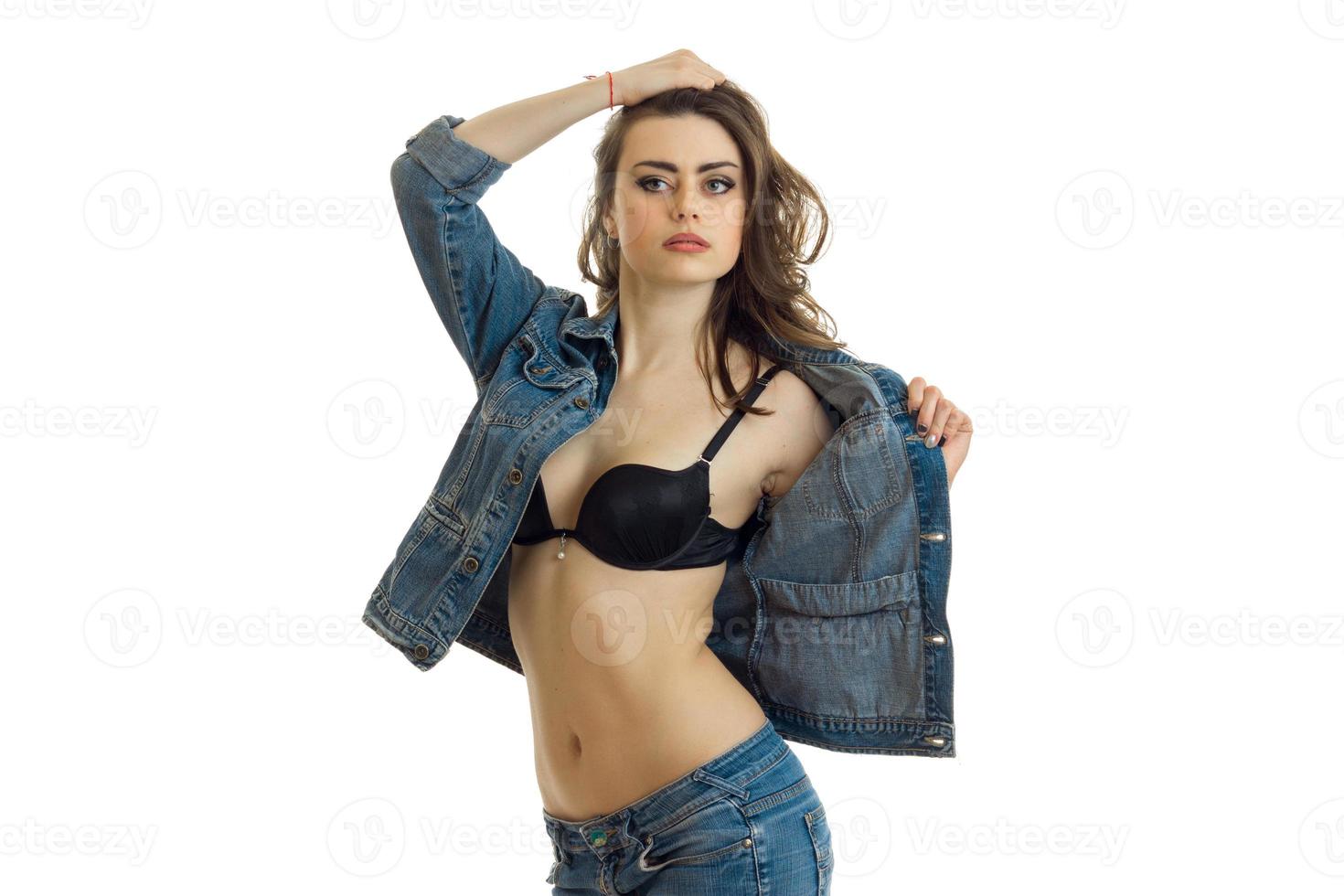 hot young brunette stands in the black bra in front of the camera and holds hand denim jacket photo