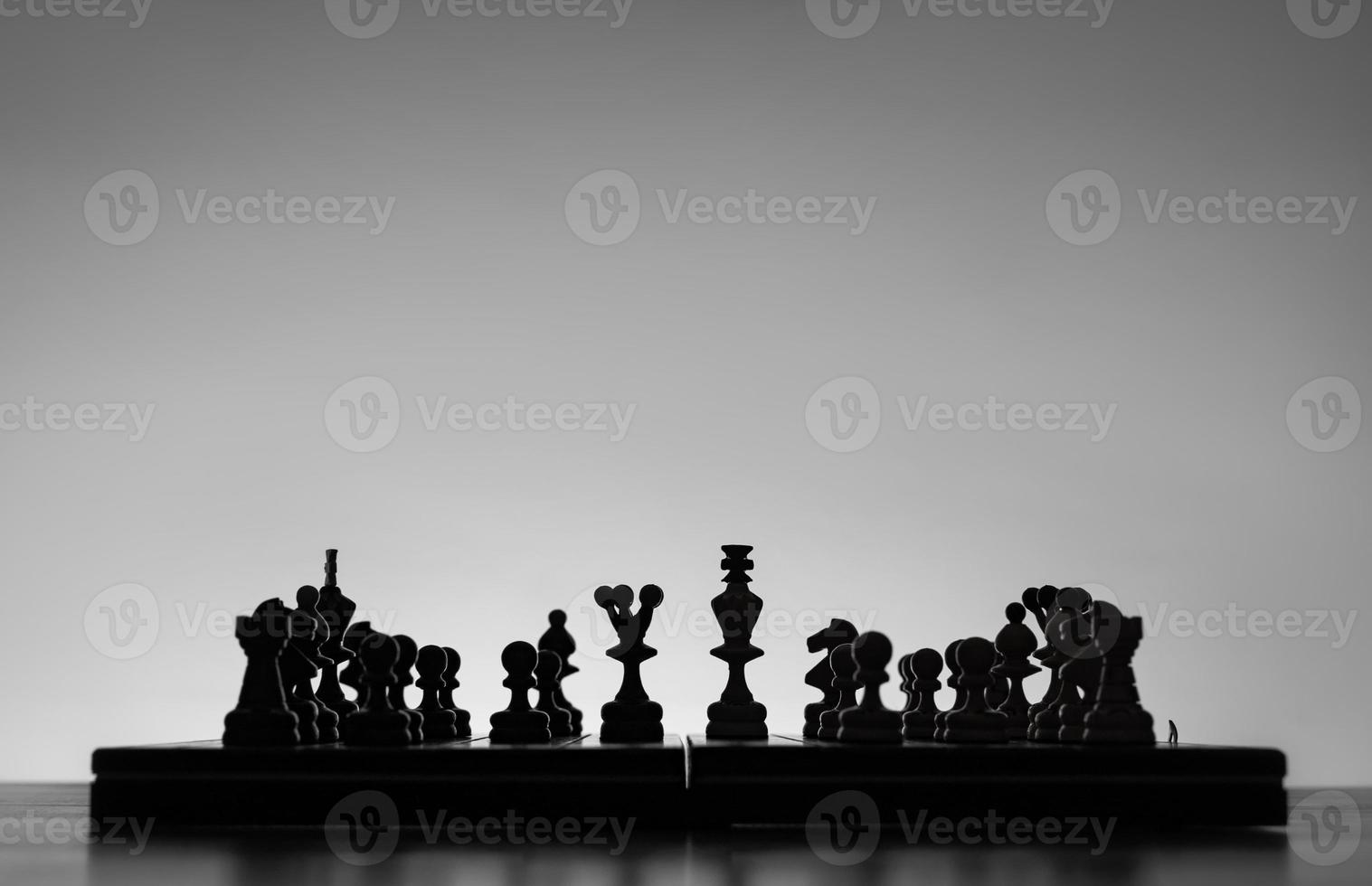 Chess board with chess pieces silhuettes on white background. Concept of business ideas and competition and strategy ideas. Black and White classic art photo. King and Queen in the middle. photo