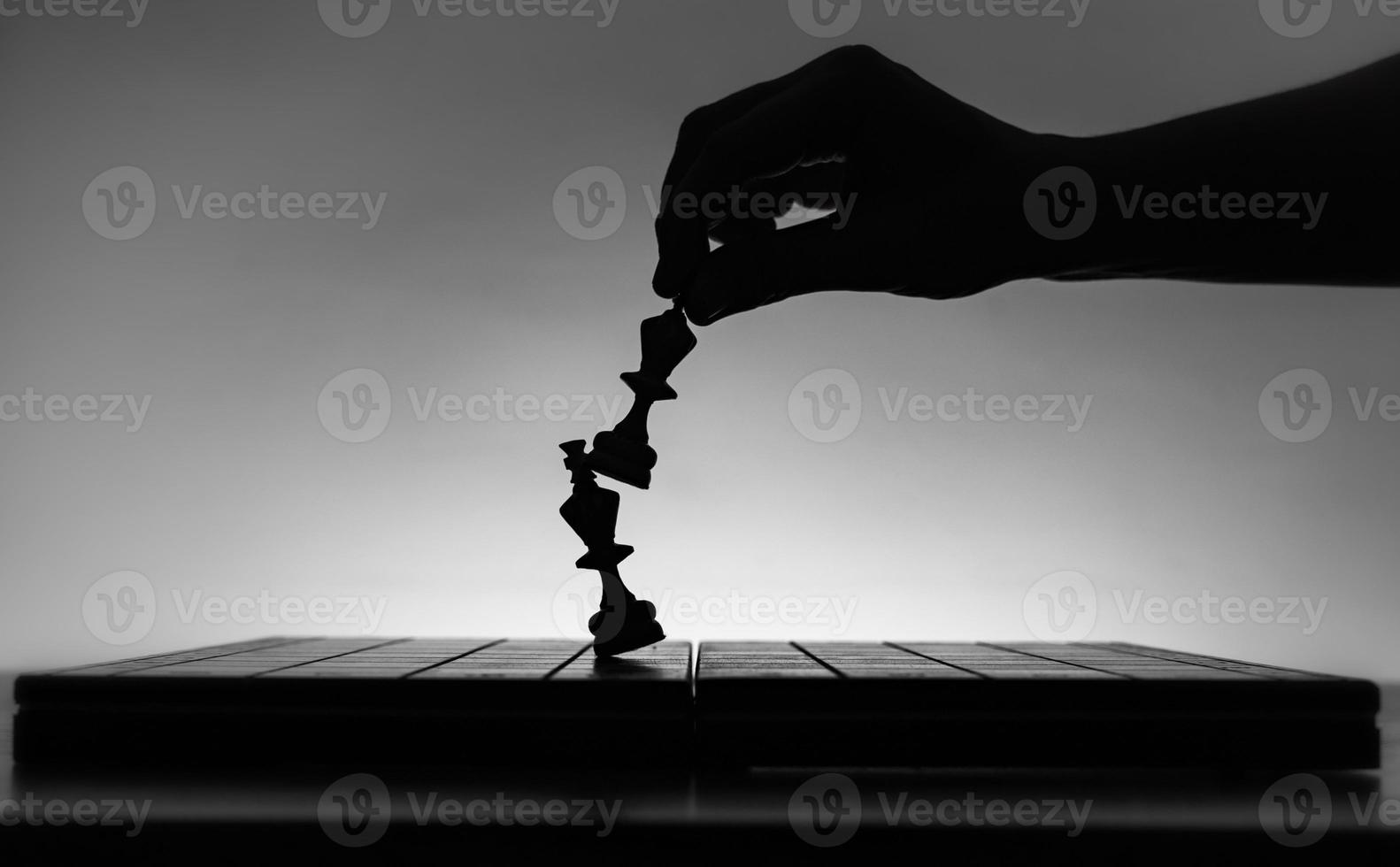 Chess board with chess pieces silhuettes on white background. Concept of business ideas, competition and strategy ideas. Black and White art photo. Chess player hand. Weak king was defeated. Checkmate photo