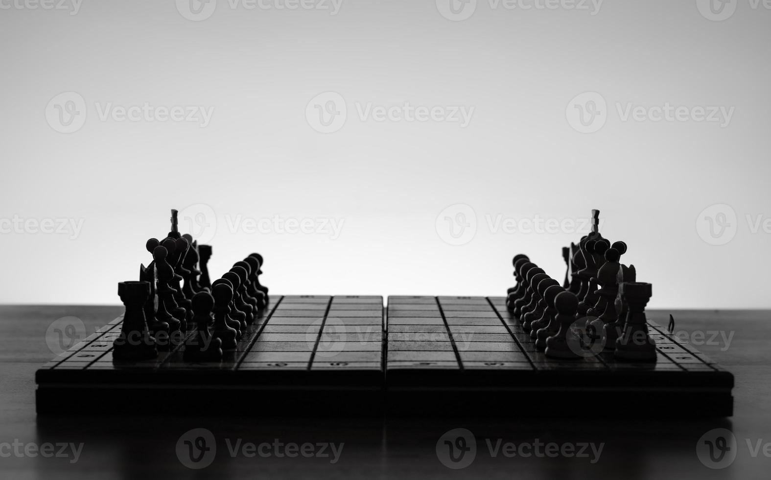 Chess board with chess pieces silhuettes on white background. Concept of business ideas, competition and strategy ideas. Black and White classic art photo. All figure ready for battle, before opening photo