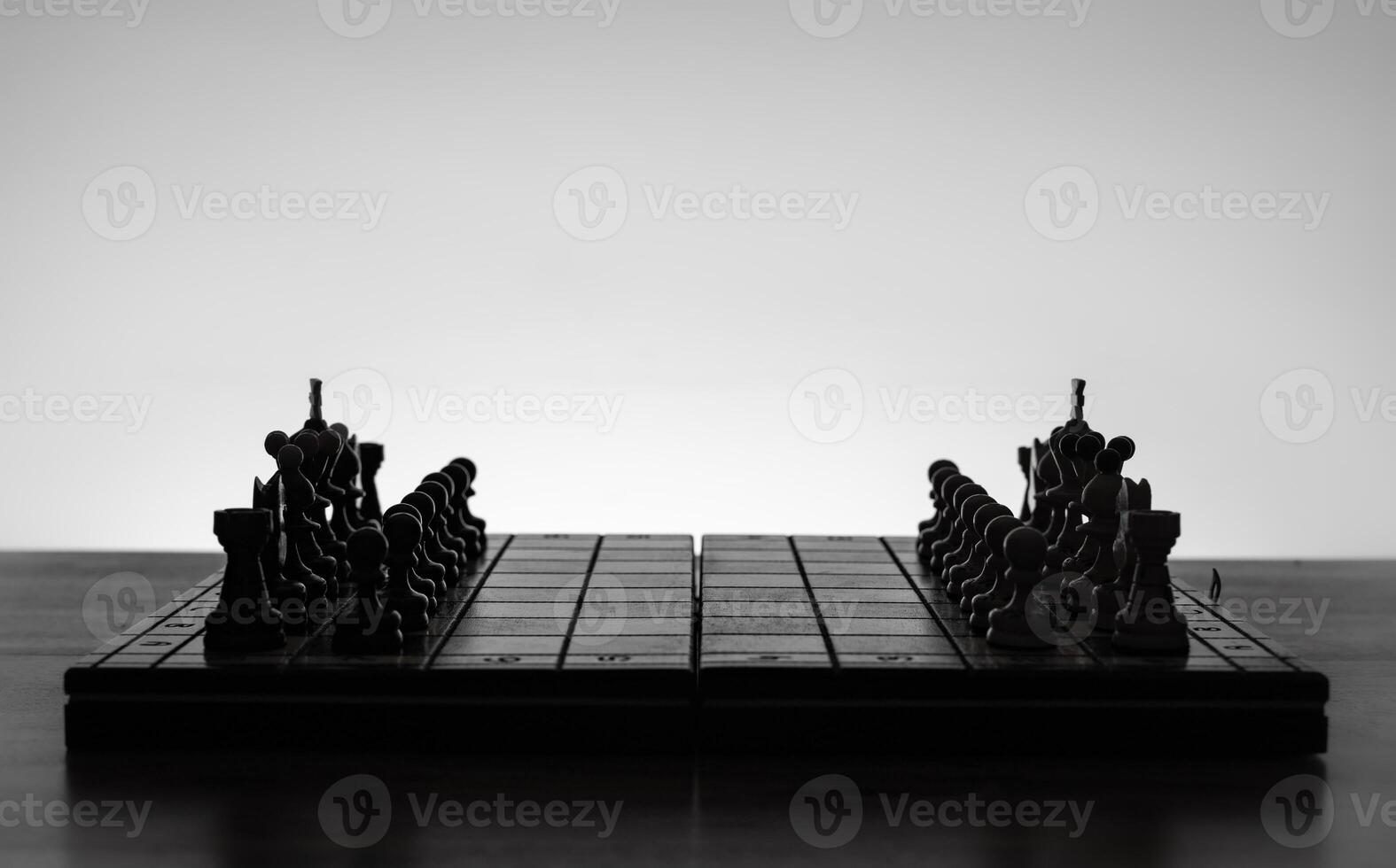 Chess board with chess pieces silhuettes on white background. Concept of business ideas, competition and strategy ideas. Black and White classic art photo. All figure ready for battle, before opening photo