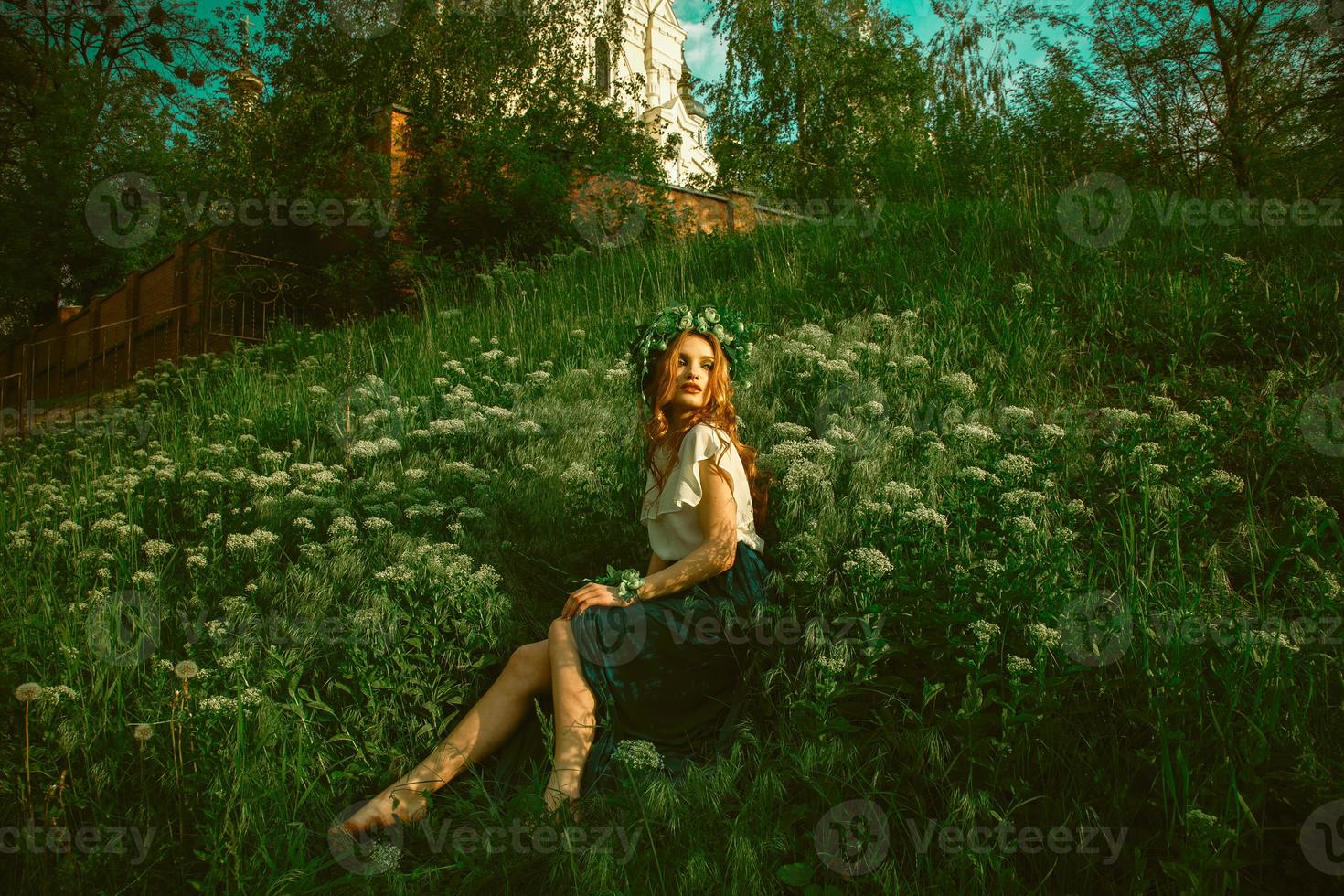 woman sits in the grass with wreath on head photo