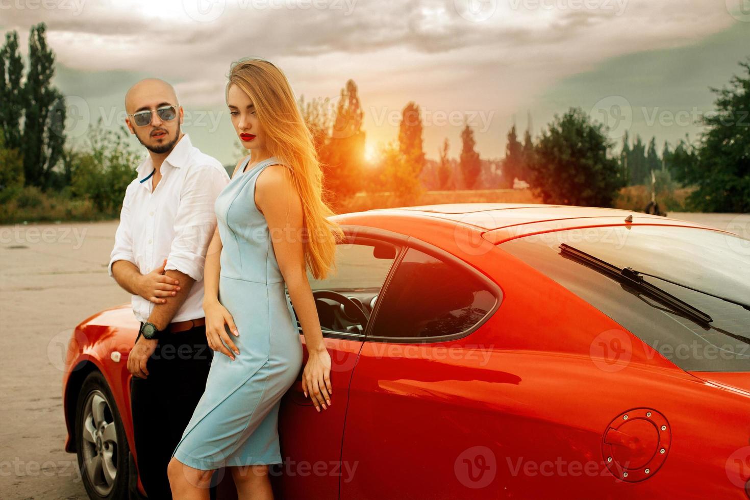 girl with man posing at sunset with sport car photo