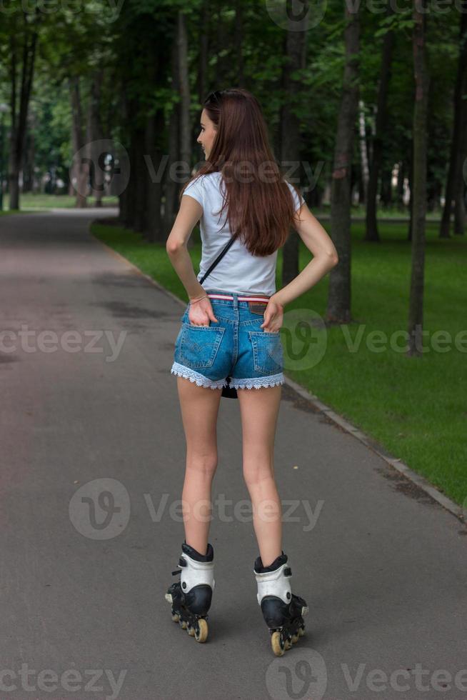 adolescente morena delgada en pantalones cortos de mezclilla montando en el parque, patinando foto