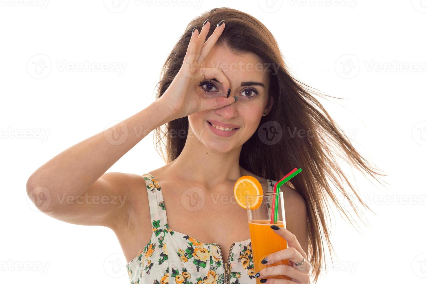 charming young brunette girl in summer clothes with floral pattern shoing OK and drinks orange cocktail isolated on white background photo