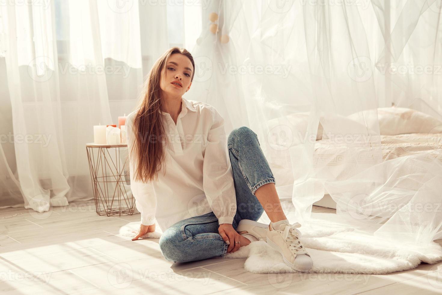 Charming woman sits in front of bed at light room at home photo