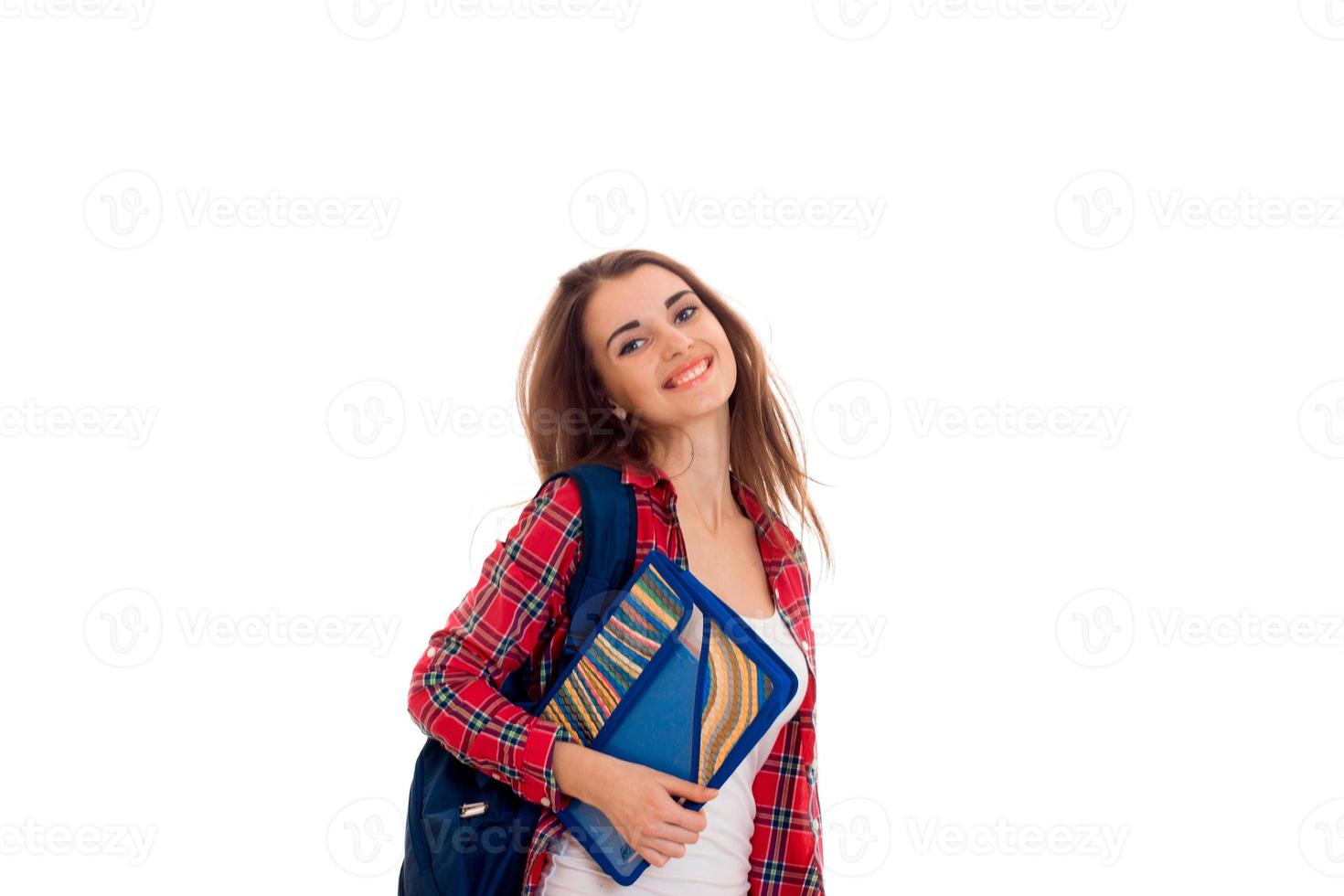 feliz y elegante estudiante inteligente con mochila en los hombros y carpetas para cuadernos en las manos posando y sonriendo en la cámara aislada en el fondo blanco foto