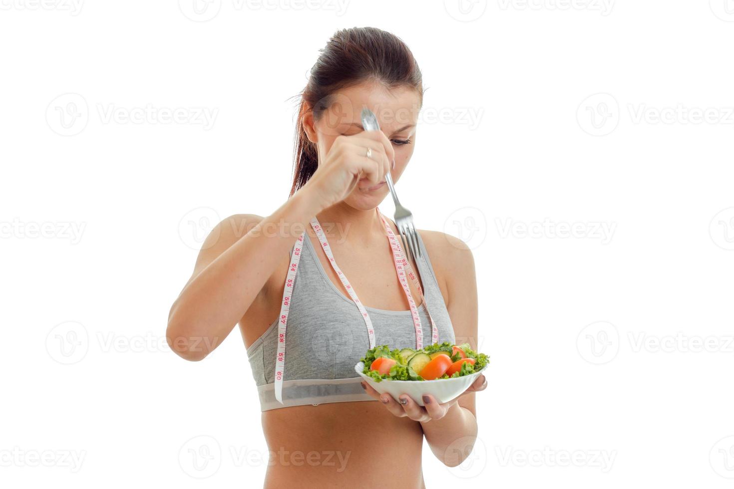 athletic girl in grey top holds a plate of salad with vegetables close-up photo