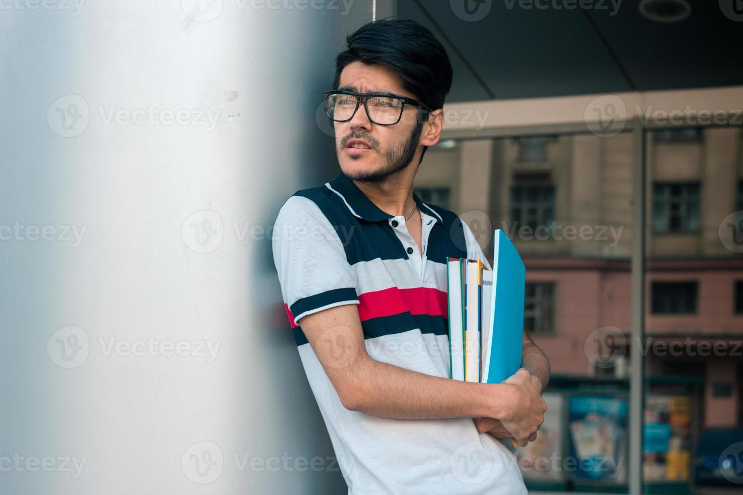 un estudiante guapo con libros en las manos usa anteojos y mira a un lado foto