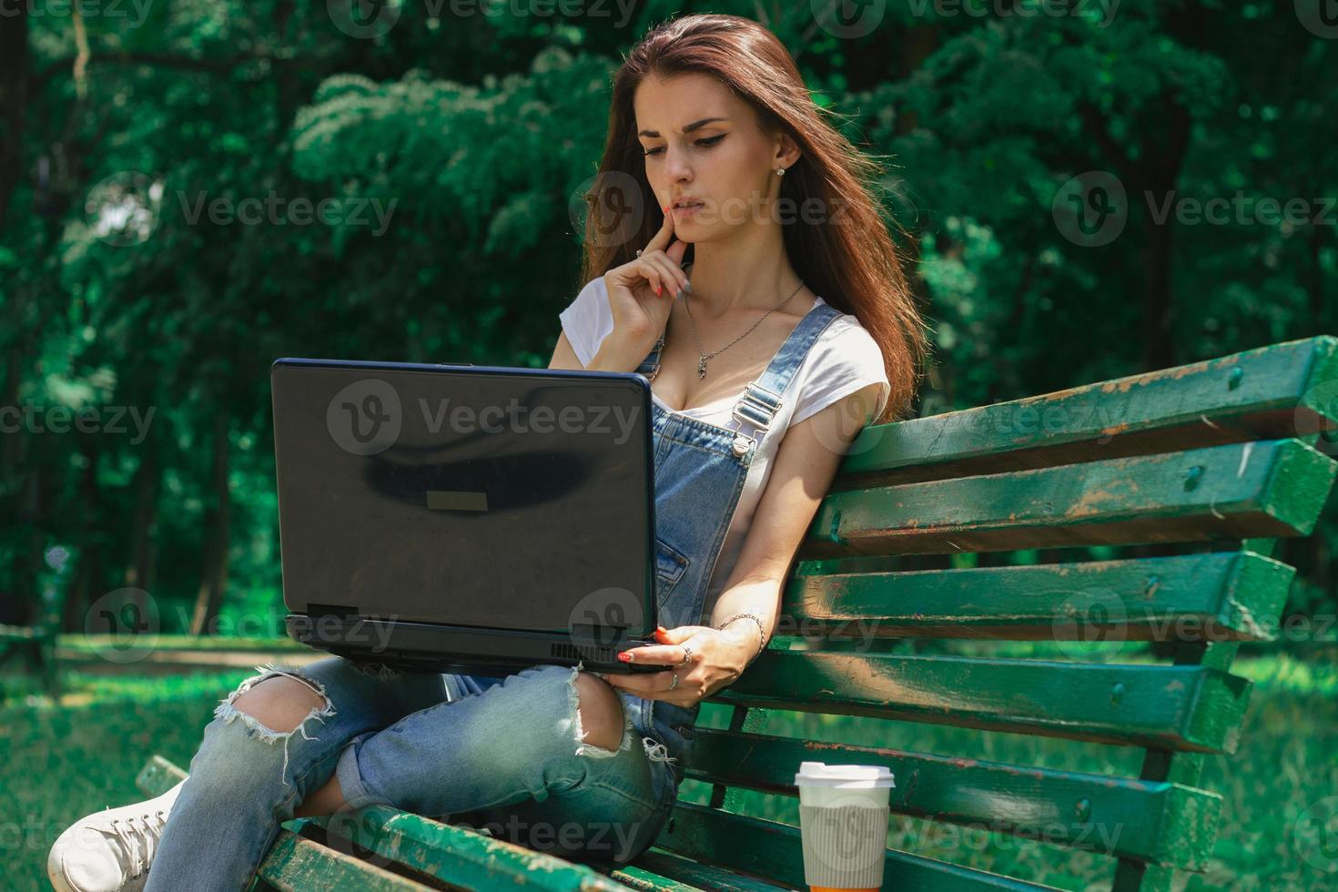 cute young girl sitting on a bench in a park with a black laptop photo