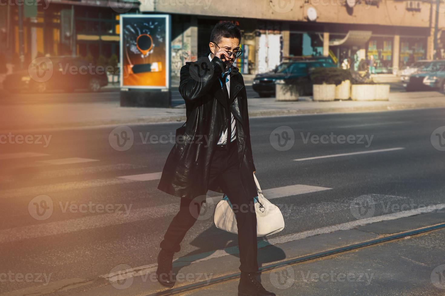 hombre con abrigo de cuero y gafas de sol cruzando la calle foto