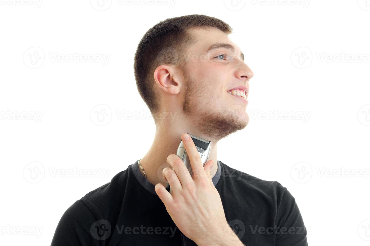 encantador joven sonriente cabeza apuntando hacia y se afeita un primer plano de la recortadora de barba foto