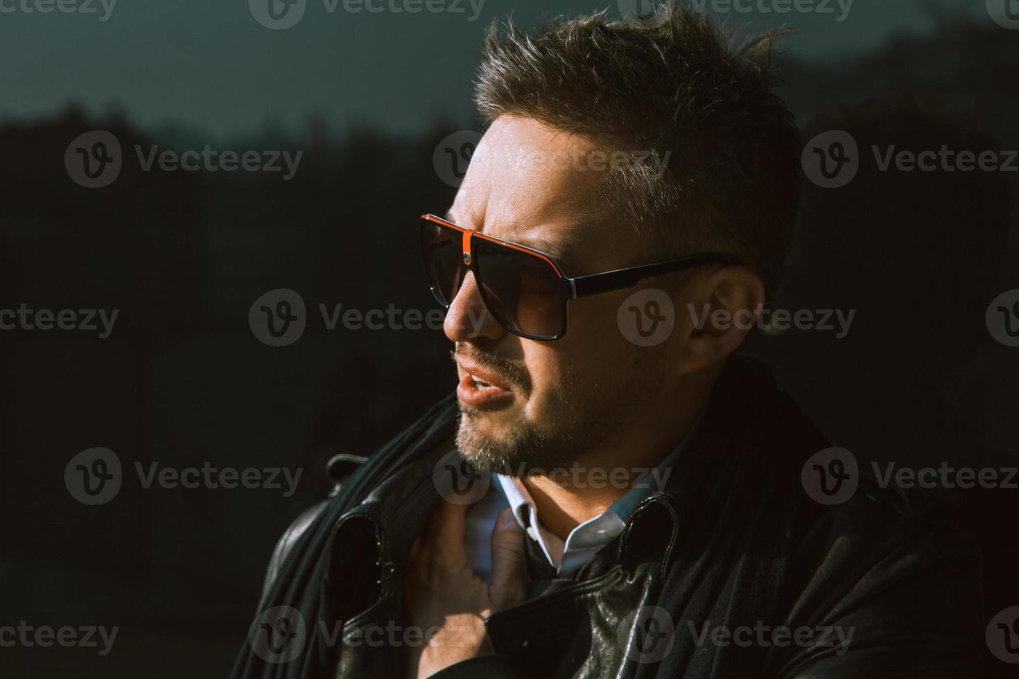 Gorgeous man in sunglasses looking aside near black wall photo