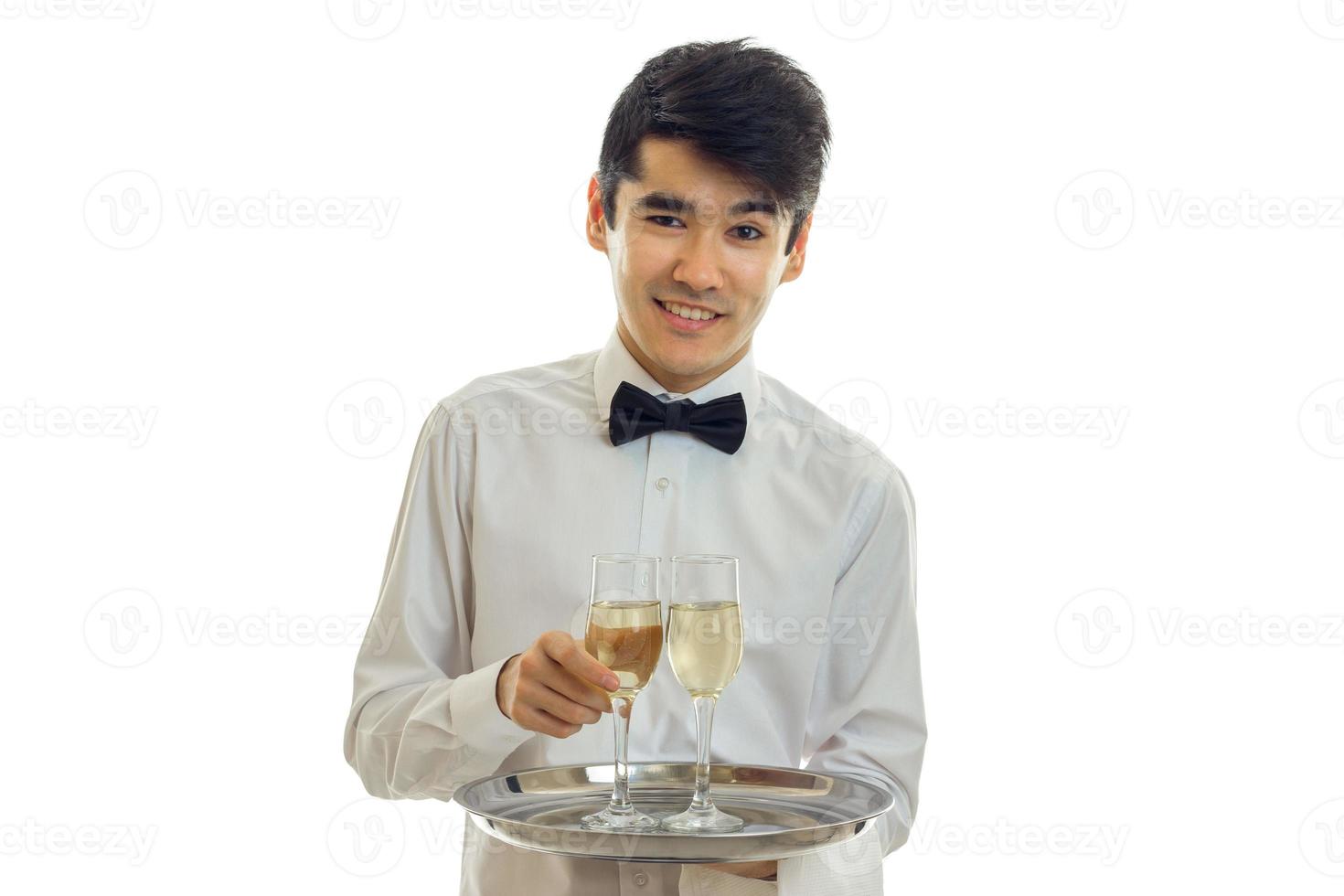 joven camarero encantador mira sonrisas rectas y sostiene una bandeja con dos copas de vino foto
