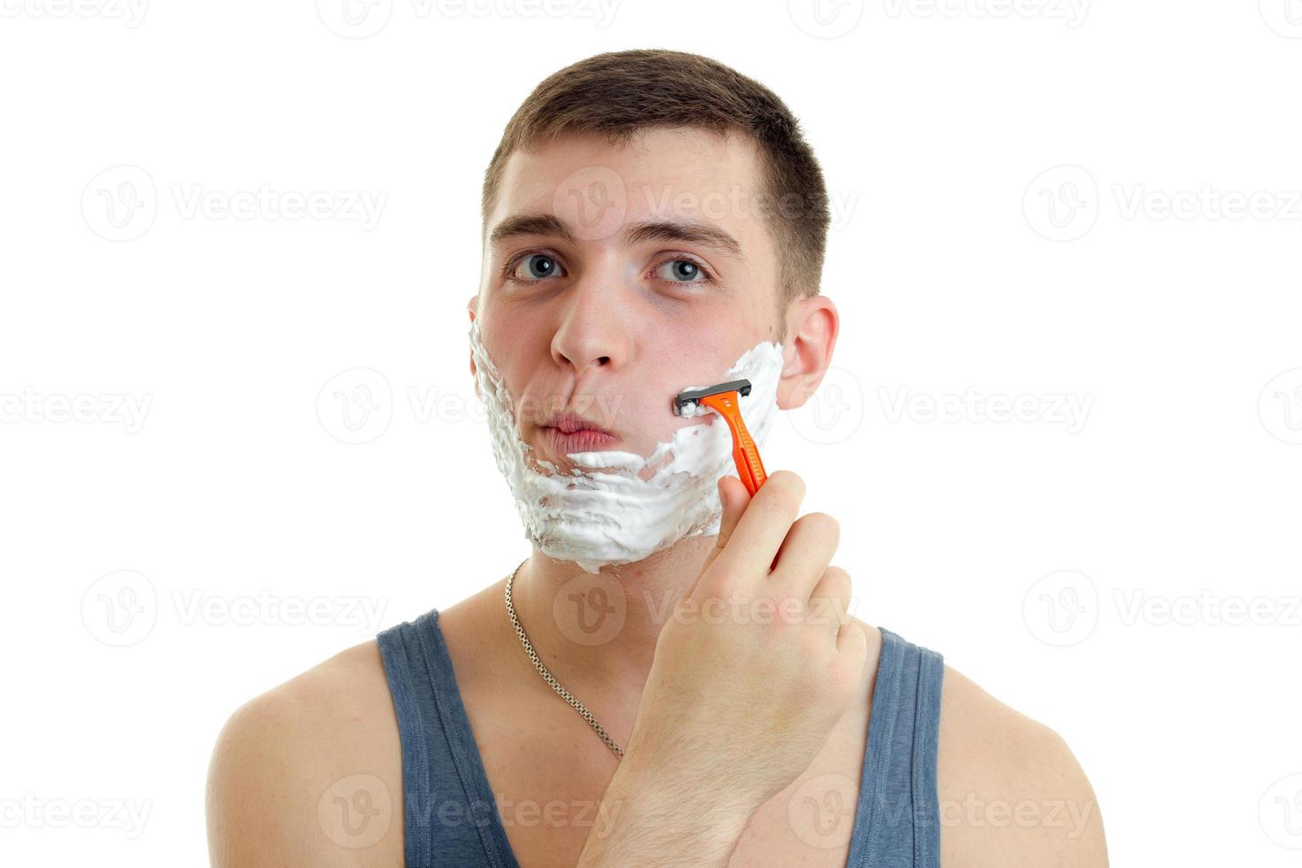 Portrait of a ridiculously young guy with foam on his face who shaves his beard machine photo