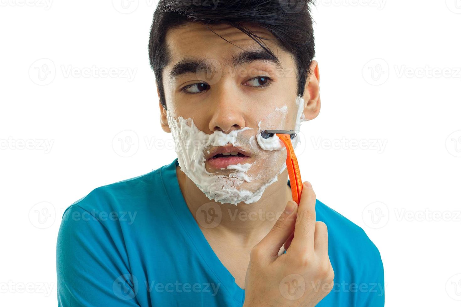 a close-up portrait of young guy who shaves his beard looks toward the machine photo