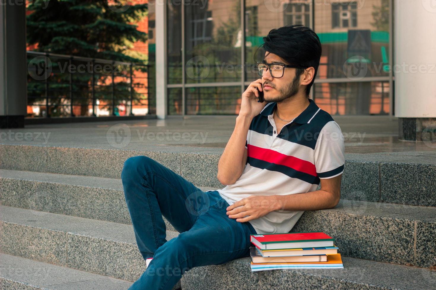 young handsome guy in glasses and books sitting on the stairs photo