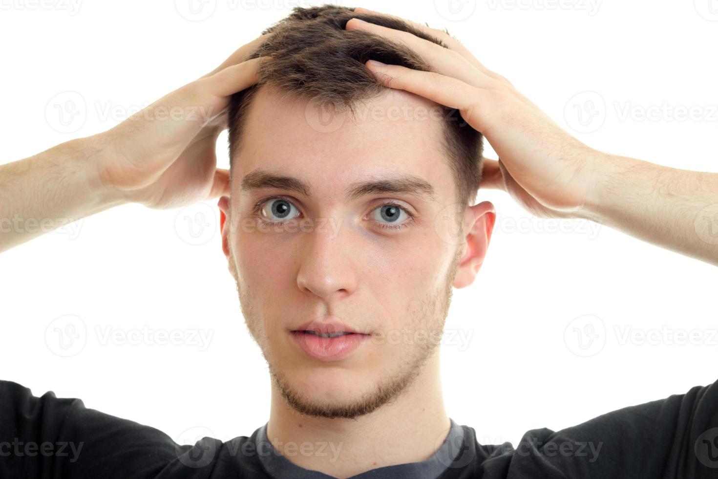 Portrait of a charming handsome guy who looks at the camera and holding up hands head isolated on white background photo