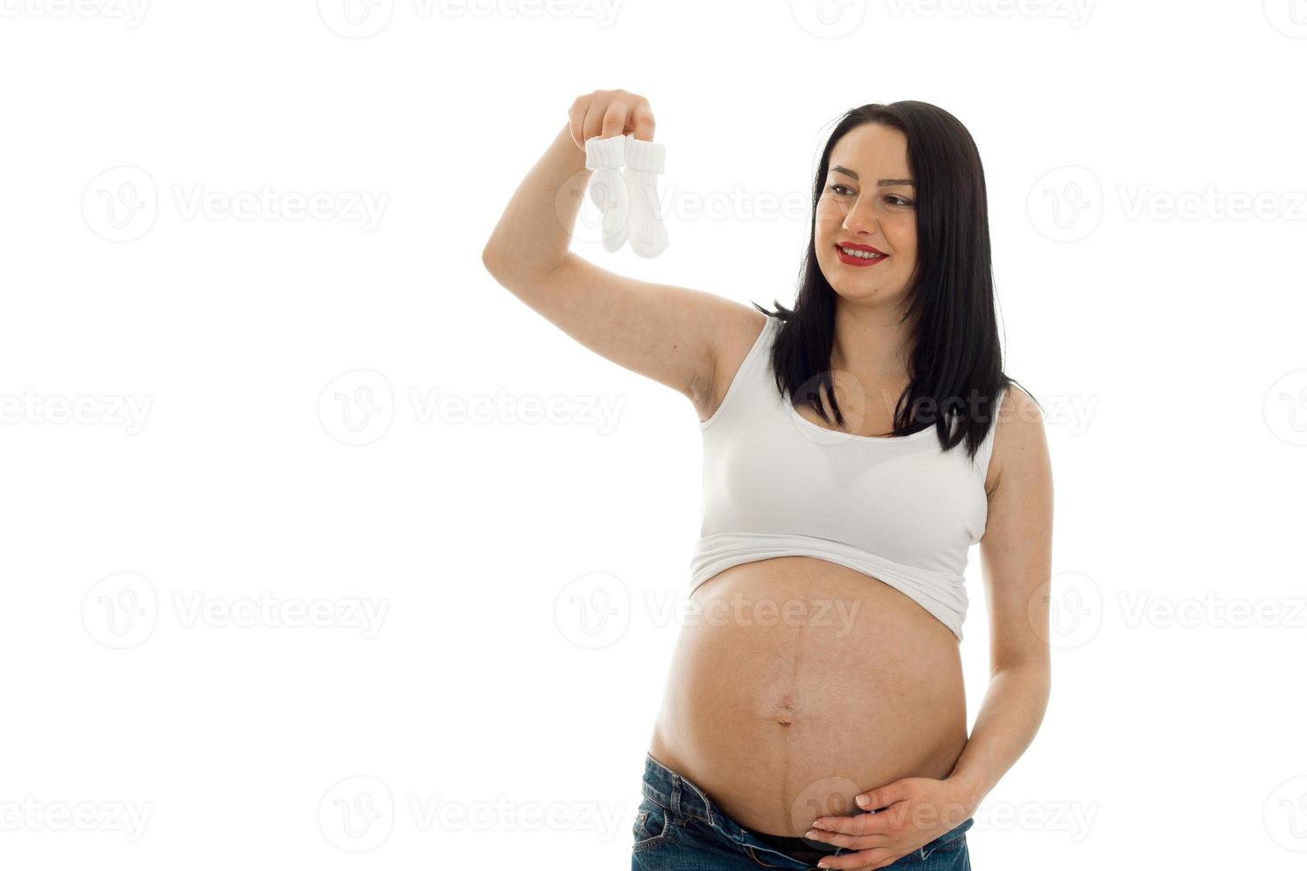 Young cheerful pregnant mother isolated on white background in studio posing with little socks in hands photo