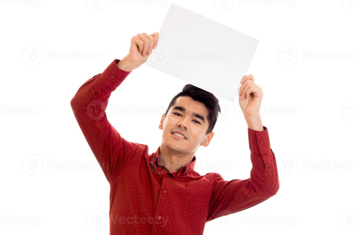Joven modelo masculino moreno feliz con camisa roja posando con una pancarta vacía en las manos y mirando y sonriendo a la cámara aislada de fondo blanco foto