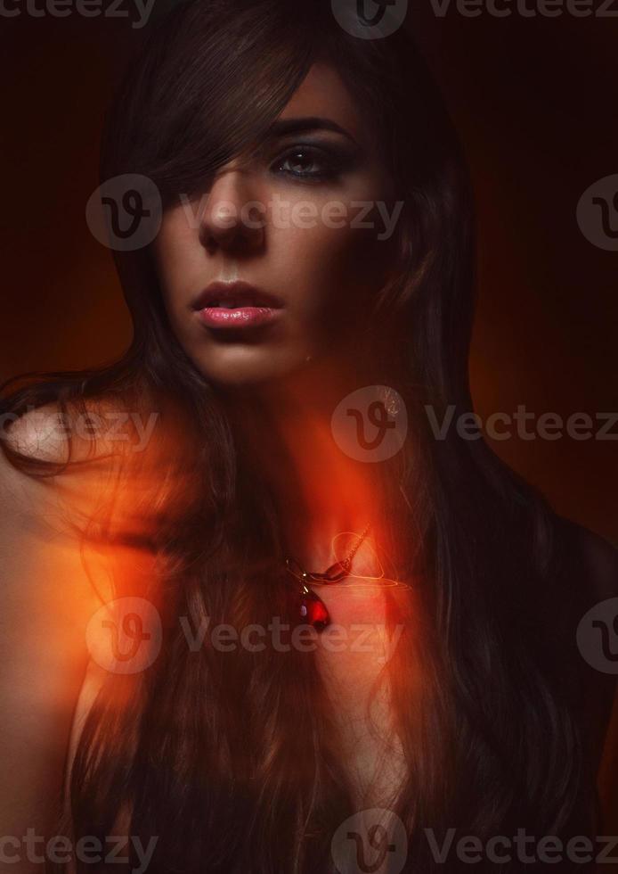 Beautiful young girl with a red jewel in the neck on a red background photo