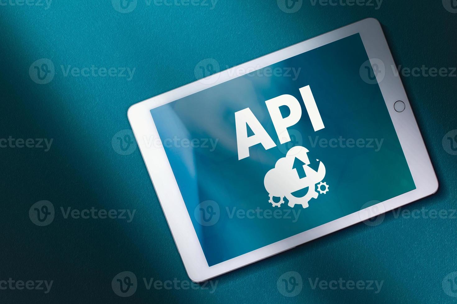 Top view of digital tablet with API acronym word on screen and teal background. Copy space. Internet and technology concept. Business, programming, interface, application and network. photo