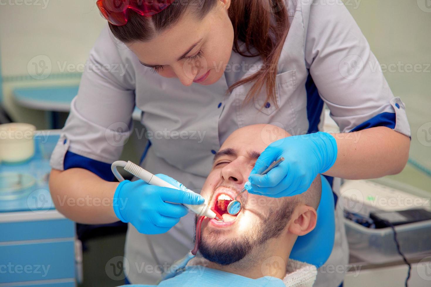 photo of handsome guy treats caries teeth in the dental office